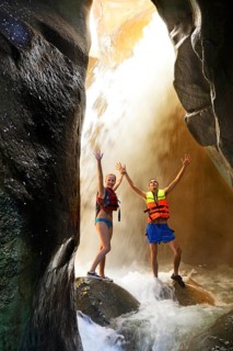 Young couple under waterfall at the canyon of Wadi Mujib