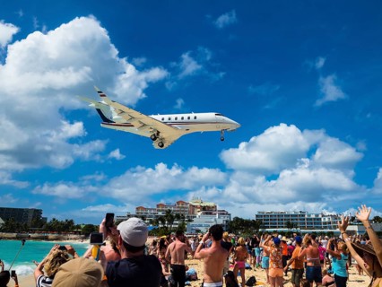 Tourists watching and photographing an airplane landing over Maho Beach