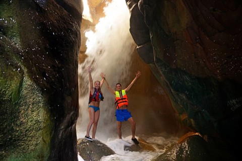 Young couple under waterfall at the canyon of Wadi Mujib