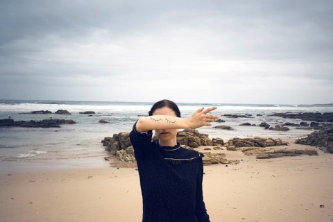Woman with closed painted on eyes on her arm standing on the beach