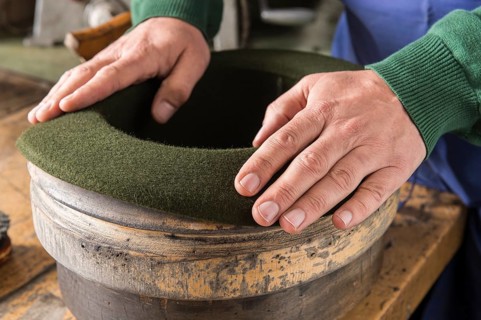 Hands shaping dry wool felt hat over edge mold