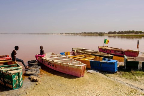 Two young women sitting on colourful wooden boats at Lac Rose