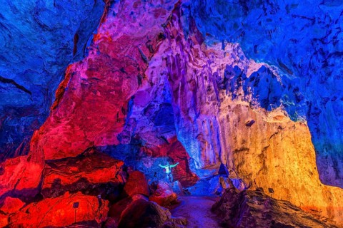 Man in a colourfully illuminated stalactite cave with stalagmites and stalactites