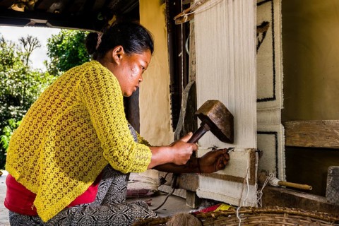 Native woman knotting carpet using sheep's wool in front of house
