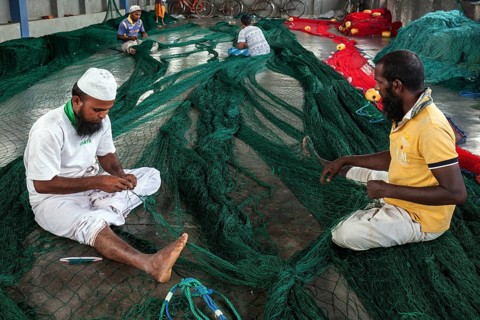 Local men repairing fishing nets in hall at harbour