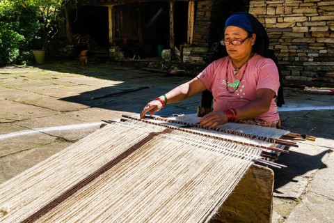 Native woman weaving blanket using sheep's wool in front of house