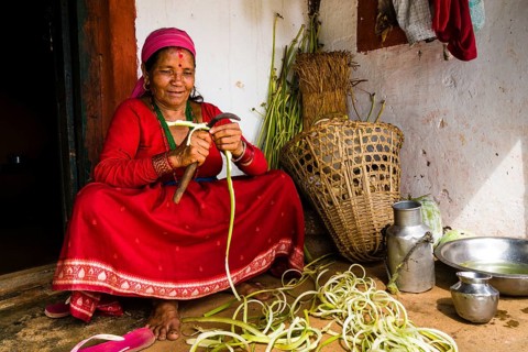 Native woman chopping vegetables in front of farmhouse