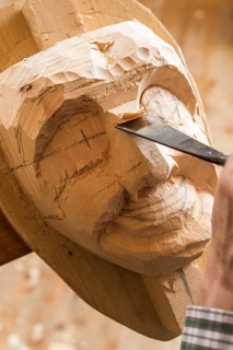 Carving the face of a wooden mask into wooden block using wood carving tools