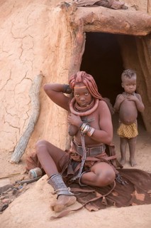 Himba woman with child in front of the mud hut