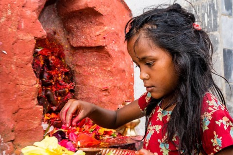 Little girl offering Prasad to statues of gods outside Khadga Devi Temple