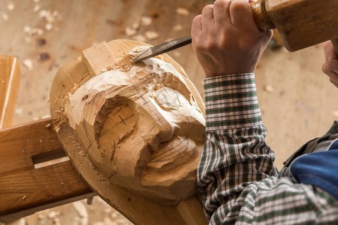 Carving the face of a wooden mask into wooden block using wood carving tools