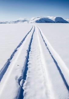 Driving tracks head off across a frozen fjord towards distant mountains
