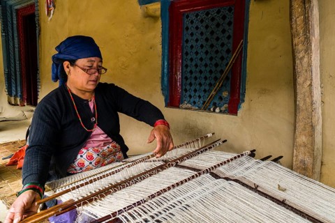 Native woman weaving blanket using sheep's wool in front of house