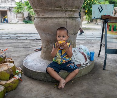Little Indonesian boy eating grilled corn on the road side