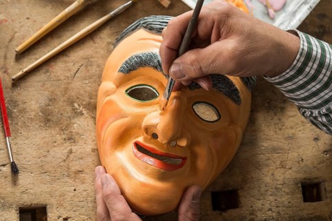 Painting the face of a wooden mask with a paintbrush