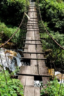 Old wooden suspension bridge across small river in Upper Modi Khola valley
