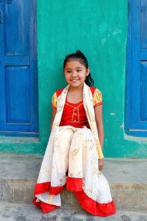 Smiling Nepalese girl seated on steps in front of a colorful house