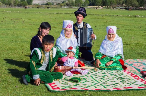 Kazakh family in traditional clothes listening to the music of an accordion player
