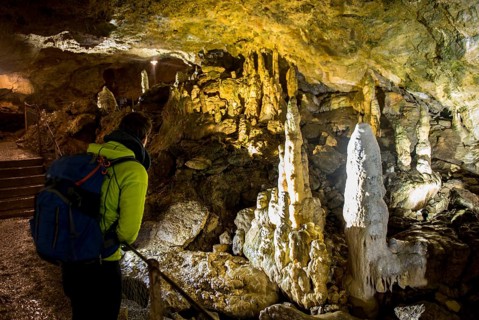 Young man looks at illuminated stalactites and stalacmites