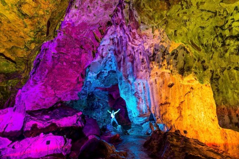 Man in a colourfully illuminated stalactite cave with stalagmites and stalactites
