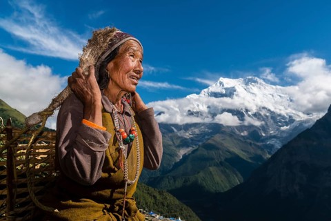 Female farmer carrying basket with harvested crops with Mount Annapurna II in the distance