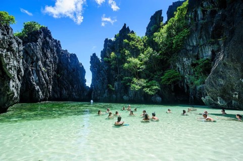 Tourists swimming in the hidden bay with crystal clear water in the Bacuit archipelago