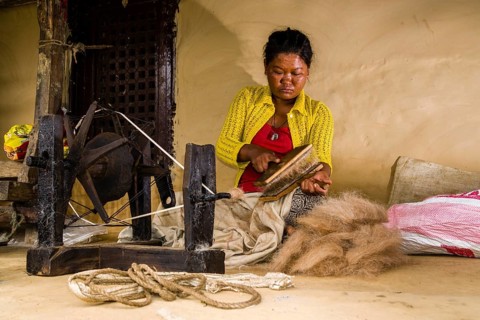 Native woman spinning sheep's wool with traditional spinning wheel in front of house