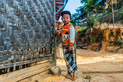 Little boy stands in front of log cabin