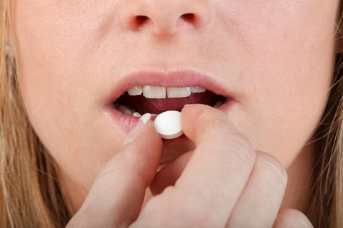 Close-up of young woman taking a pill