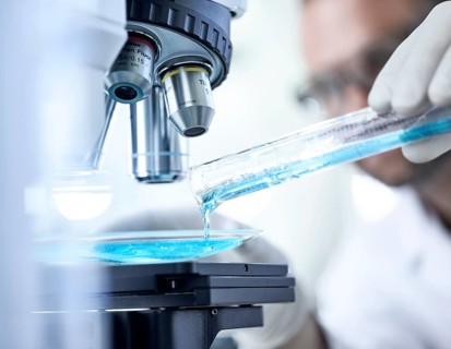 Chemist studying blue liquid under microscope