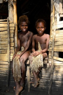 Two local children sitting in front of a hut