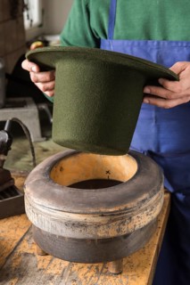 Hands holding dry wool felt hat over an edge mold