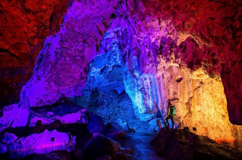 Young man looks at colorfully illuminated stalactite cave