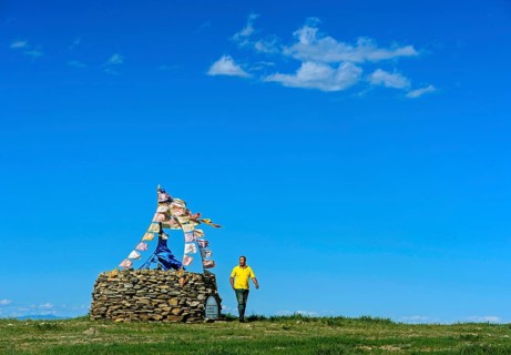 Mongolian man performing prayer ritual beside ovoo