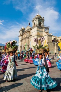 Women in traditional dresses with flower baskets dancing on the main square Zocalo in front of church Santo Domingo de Guzman