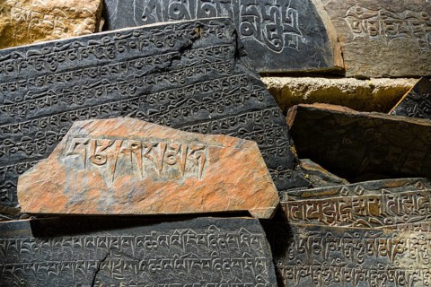 Mani stones with the engraved tibetan mantra Om Mani Padme Hum are piled up to a wall