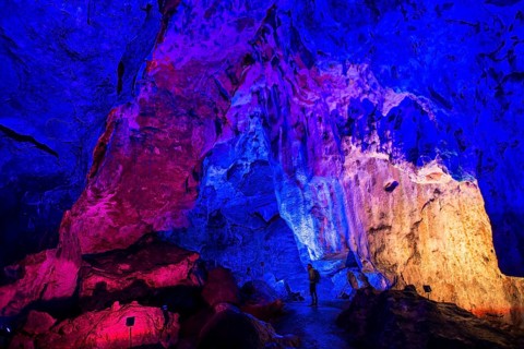 Young man looks at colorfully illuminated stalactite cave