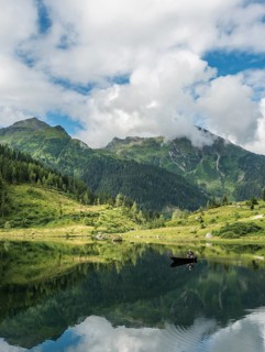 Fisherman on Lake Riesachsee with reflection of forest and mountains