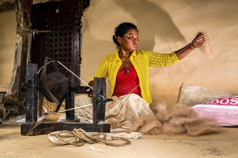 Native woman spinning sheep's wool with traditional spinning wheel in front of house
