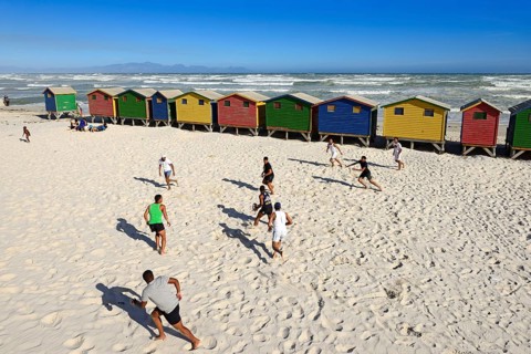 Teenagers play rugby in front of colourful beach houses