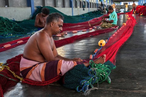 Local men repairing fishing nets in hall at harbour