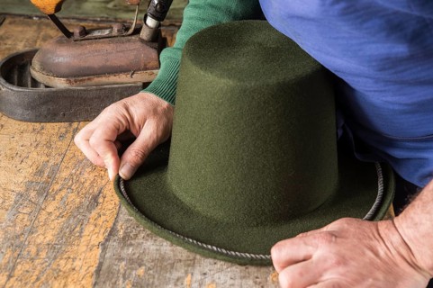 Hands holding cord on dry wool felt hat with shaped edge
