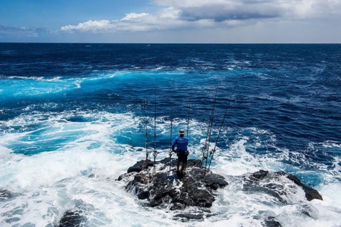 Fisherman standing on a rock in The Sea with his angling rods