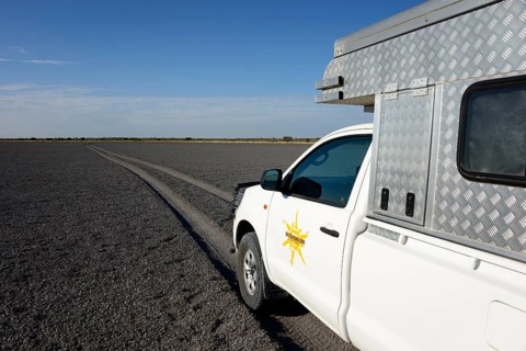 Truck with camper driving through Deception Pan in Deception Valley of the Central Kalahari Game Reserve