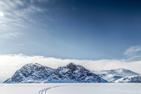Driving tracks head off across a frozen fjord towards distant mountains