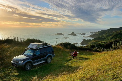 Woman sitting with off-road vehicle at the coast