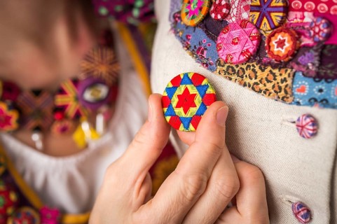 Button maker's hand fits the finished Posamentenknopf to Dirndl on a doll