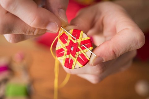 Button maker stitching and wrapping red and yellow yarn into star pattern