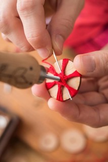 Button maker in third step of Posamentenknopfe production holding wooden blank with vise and carefully stitching and wrapping red yarn into star pattern