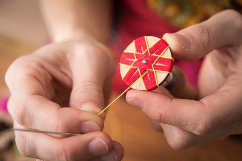 Button maker stitching and wrapping red and yellow yarn into star pattern